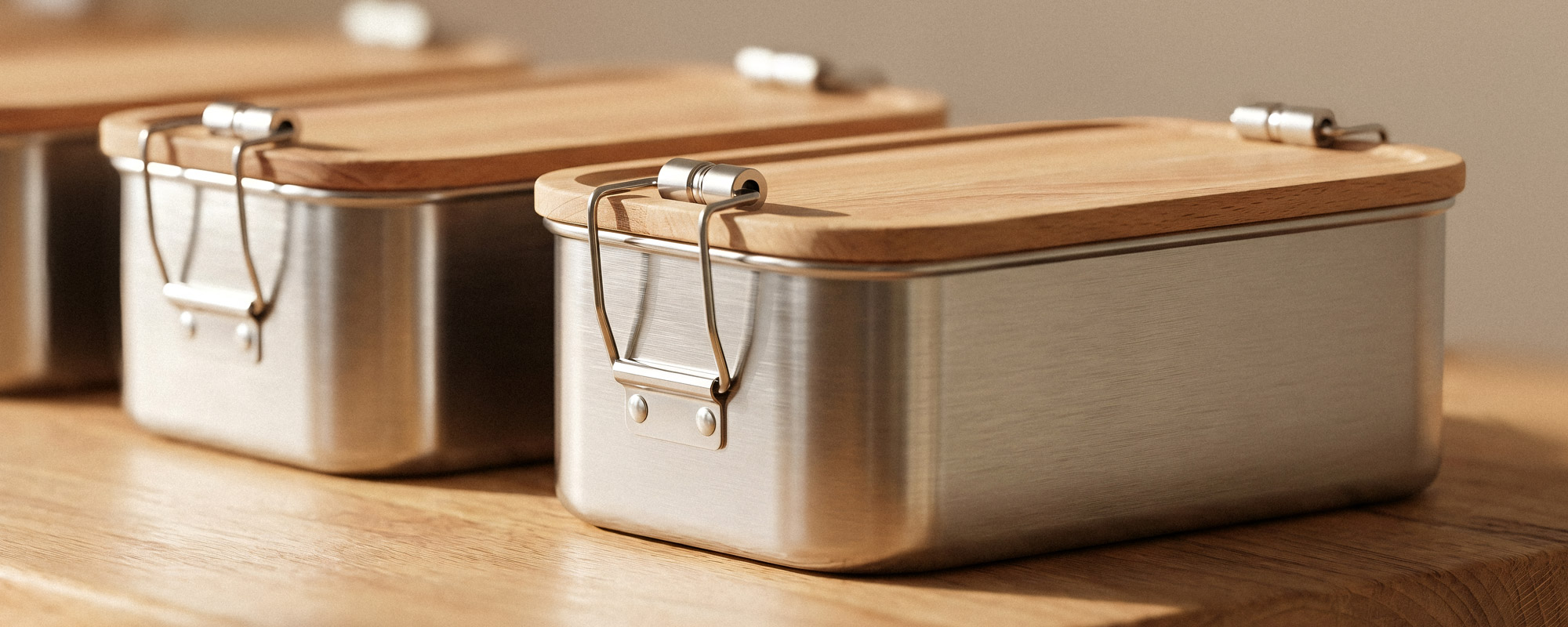 Edelstahl-Lunchboxen mit Buchenholzdeckel, Metallverschlüssen und gebürsteter Oberfläche auf Holzuntergrund.