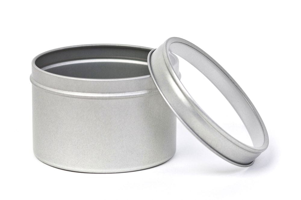 Geöffnete runde silberfarbene Kräuterdose aus Metall mit abgenommenem Deckel, der ein transparentes Sichtfenster enthält, auf weißem Hintergrund.