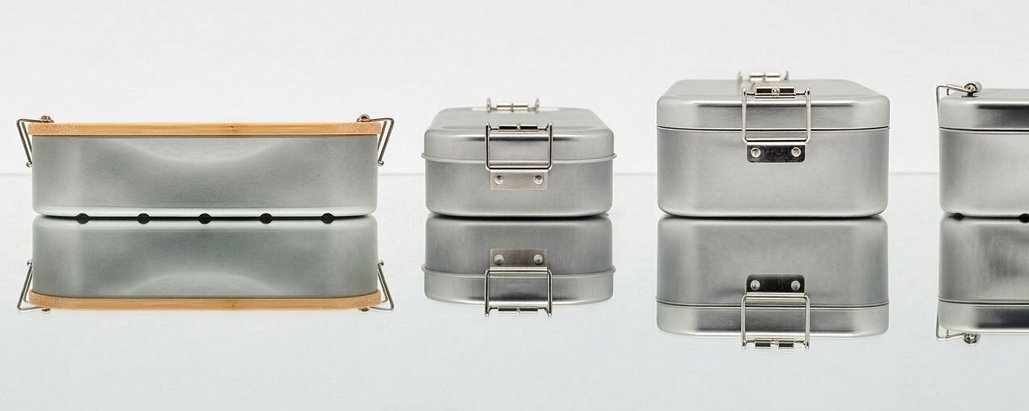 Edelstahl-Lunchboxen mit Metallverschluss und Bambusdeckel in verschiedenen Ausführungen, präsentiert auf reflektierender Oberfläche.