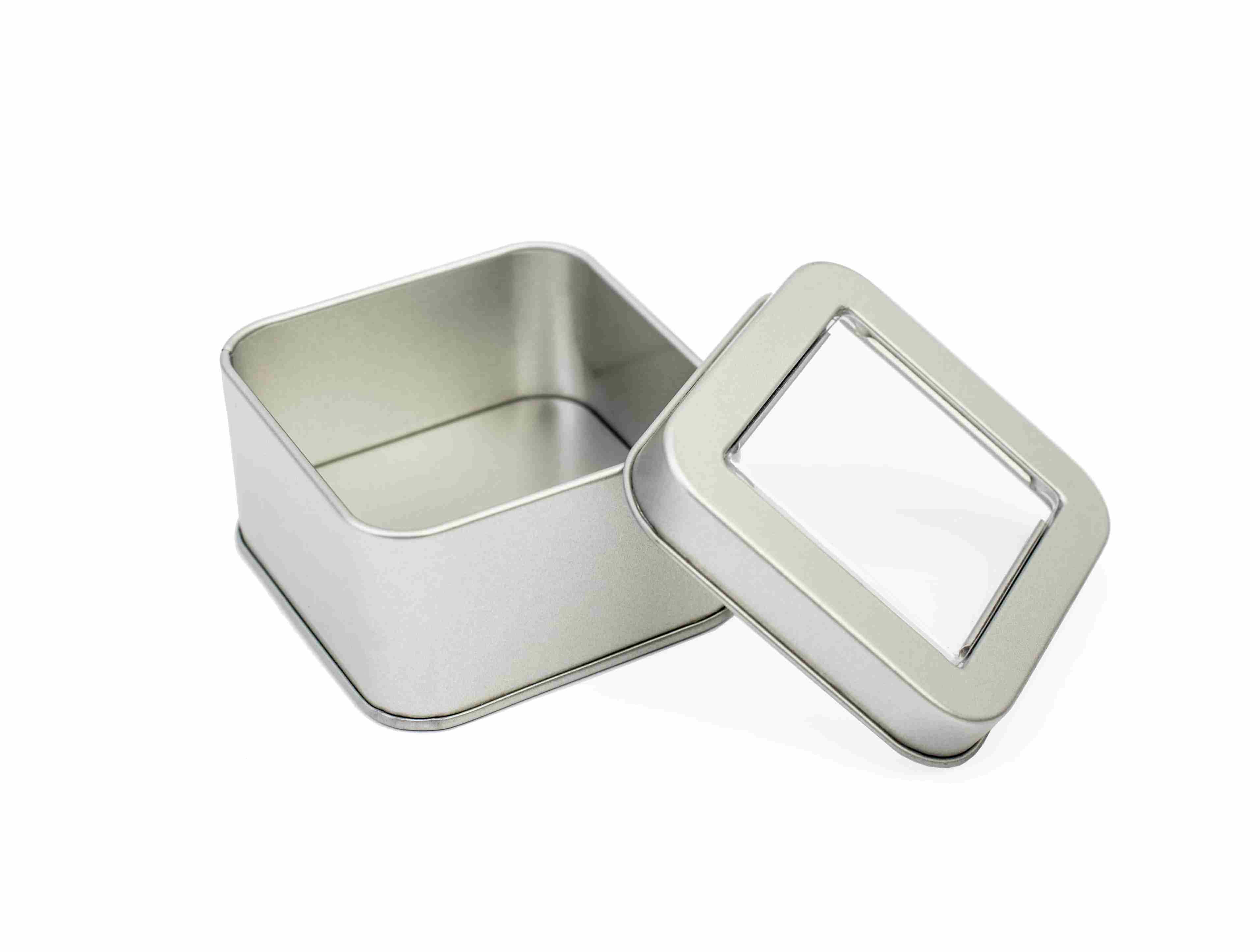 Geöffnete quadratische Metalldose in Silber mit abgenommenem Deckel, der ein transparentes Sichtfenster hat, auf weißem Hintergrund fotografiert.