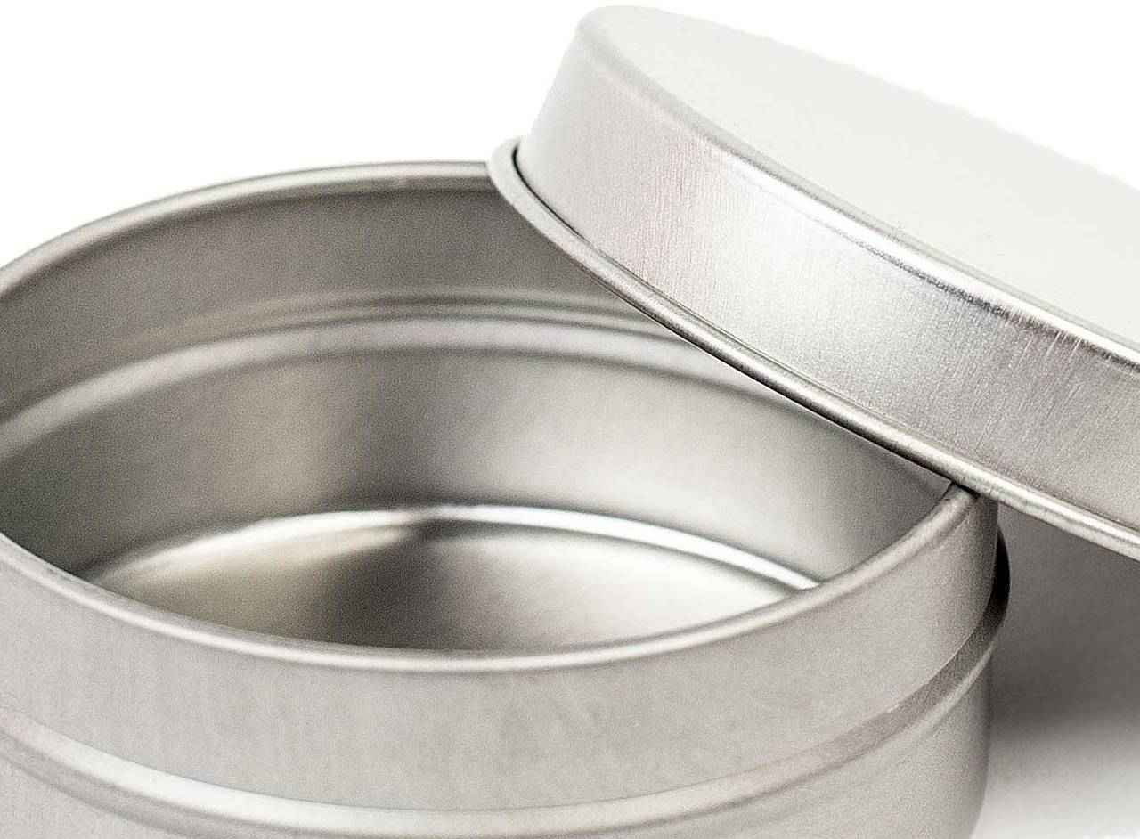 Geöffnete kleine runde flache Blechdose mit abgenommenem Stülpdeckel, die Innenfläche ist sichtbar, auf weißem Hintergrund.