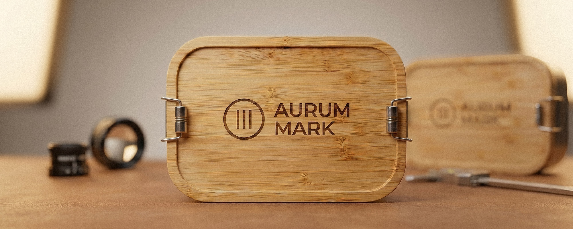 Bambusdeckel einer Edelstahl-Dose mit gelaserter „AURUM MARK“-Gravur und Metallverschlüssen; hochwertige Produktaufnahme mit Fokus auf natürliche Materialien.
