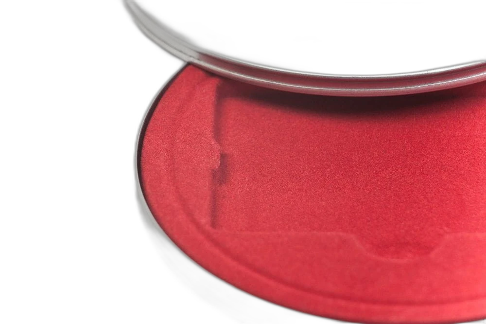 Detailansicht einer runden silberfarbenen Metalldose mit teilweise geöffnetem Deckel, innen mit rotem Samteinsatz.