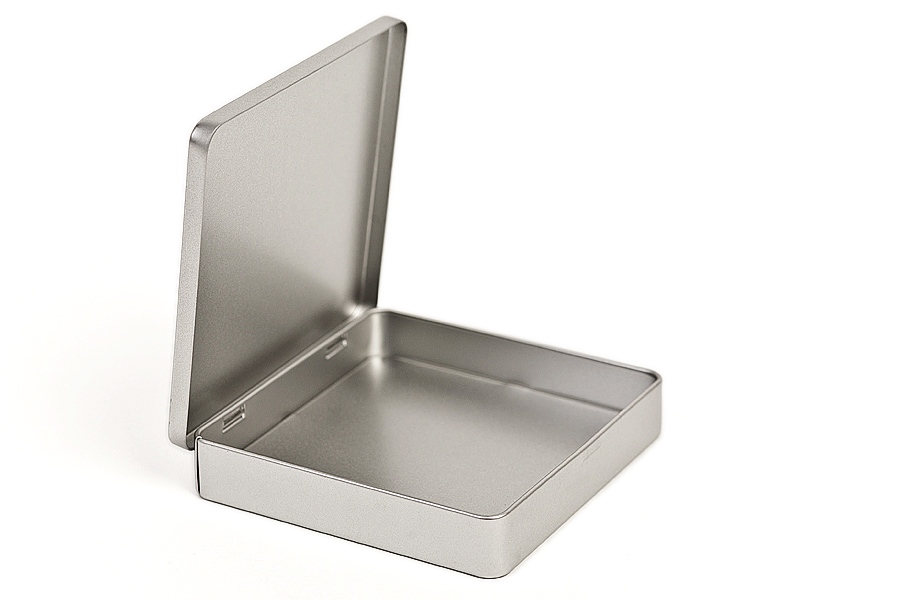 Geöffnete quadratische Schokoladendose aus silberfarbenem Metall, ohne Deckel, auf weißem Hintergrund fotografiert.