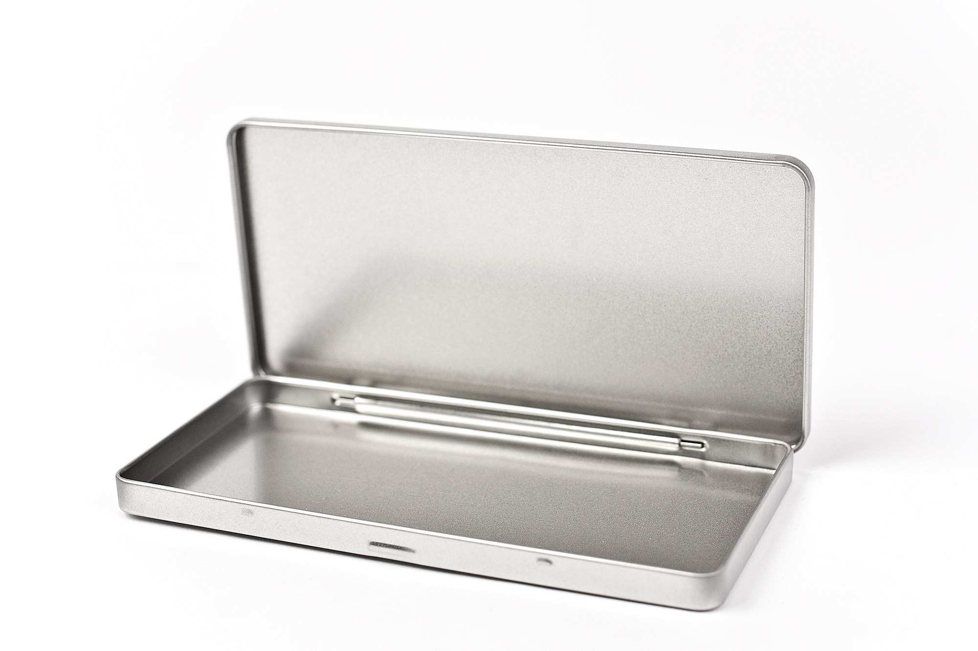 Geöffnete eckige Blechdose aus silberfarbenem Metall mit Scharnierdeckel, auf weißem Hintergrund. Der Deckel ist vollständig geöffnet und zeigt den Innenraum der Dose.