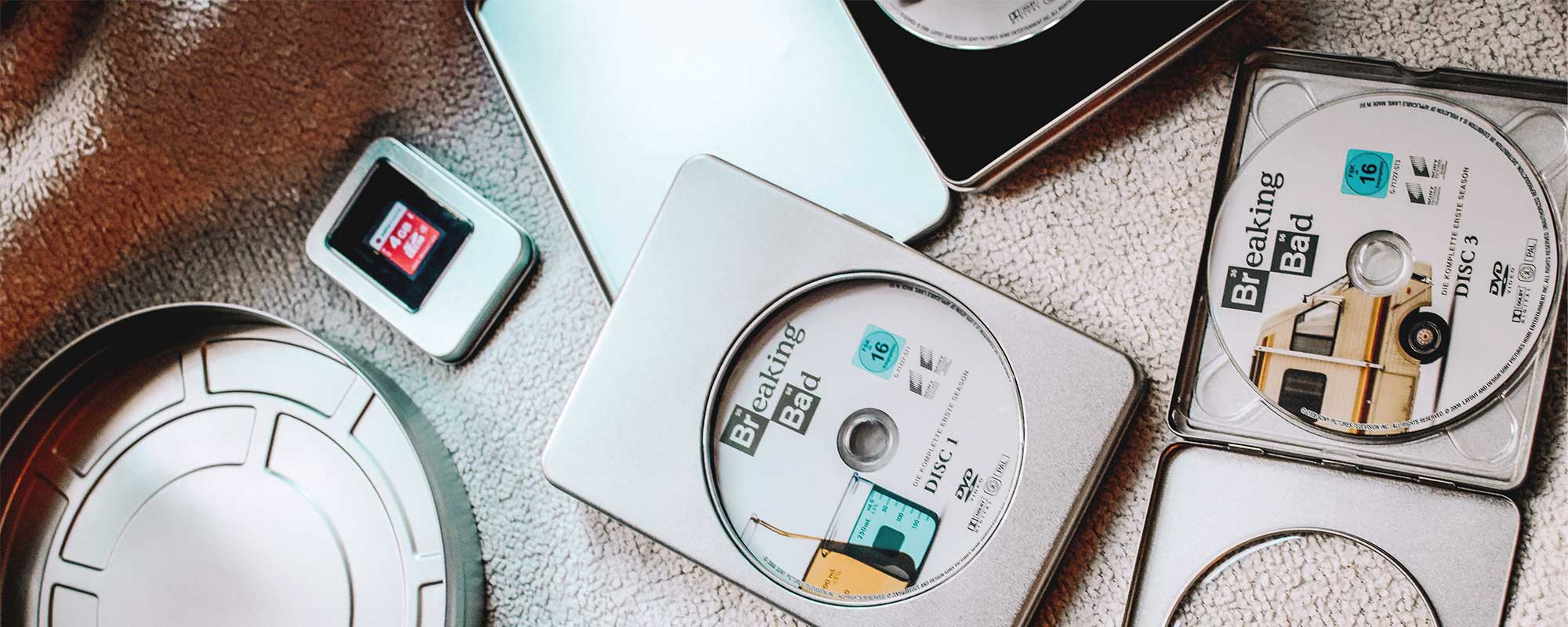 Mediendosen aus Metall mit DVDs und Sammlermotiven, geöffnet mit Disc-Inhalten und Zubehör auf strukturierter Oberfläche.