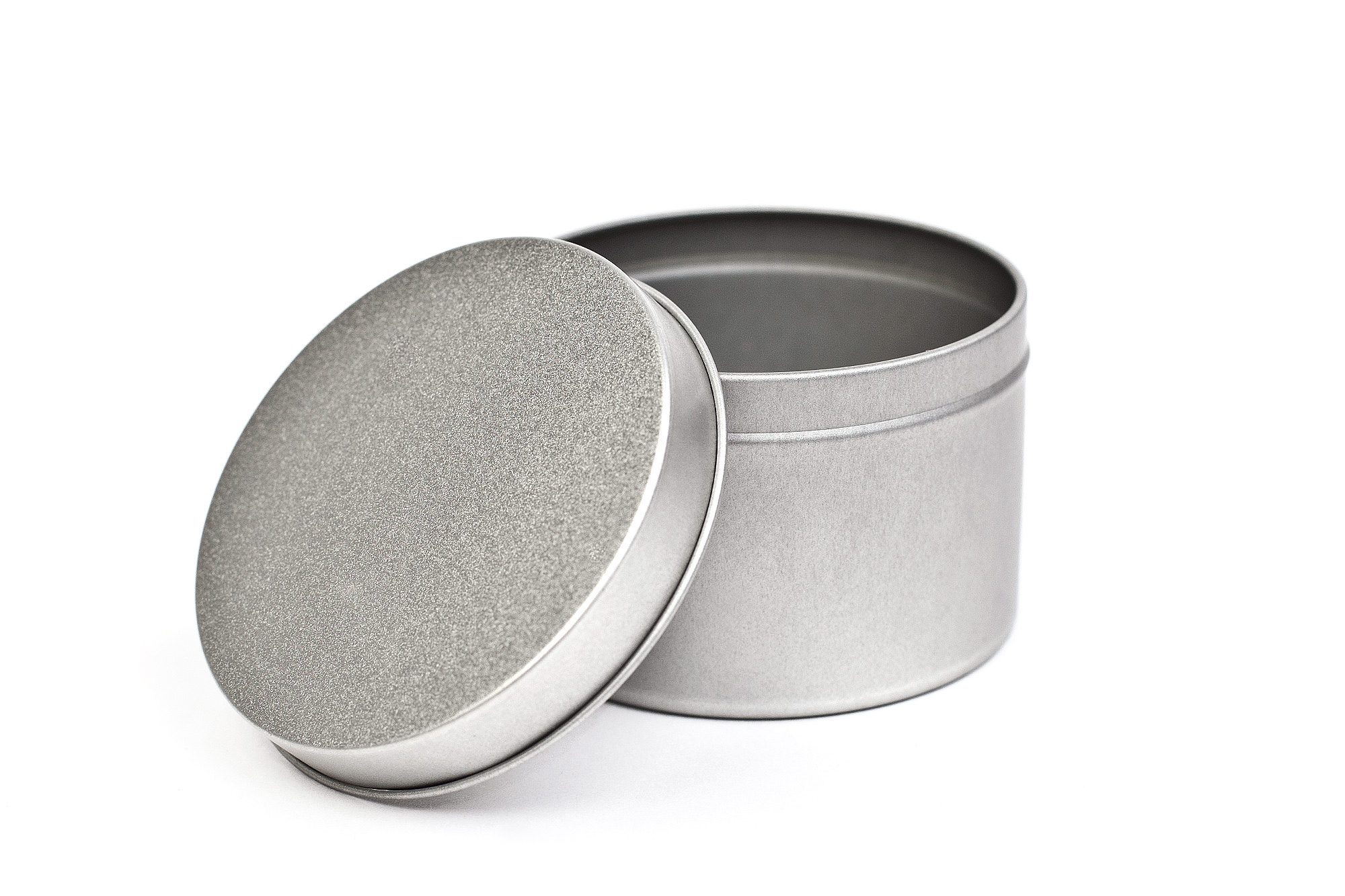 Geöffnete runde Blechdose mit Stülpdeckel aus Metall, der leicht schräg an die Dose gelehnt ist. Die Dose ist leer und silberfarben.