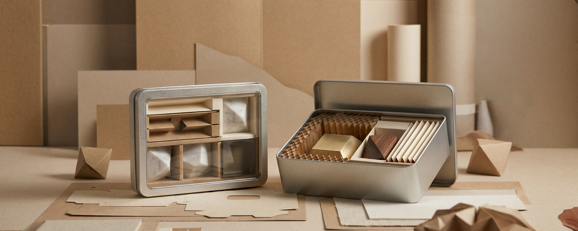Zwei offene silberne Metalldosen mit Karton- und Papier-Inlays sowie geometrischen Formen; minimalistische Produktaufnahme mit natürlichen Materialien und warmen Erdtönen.