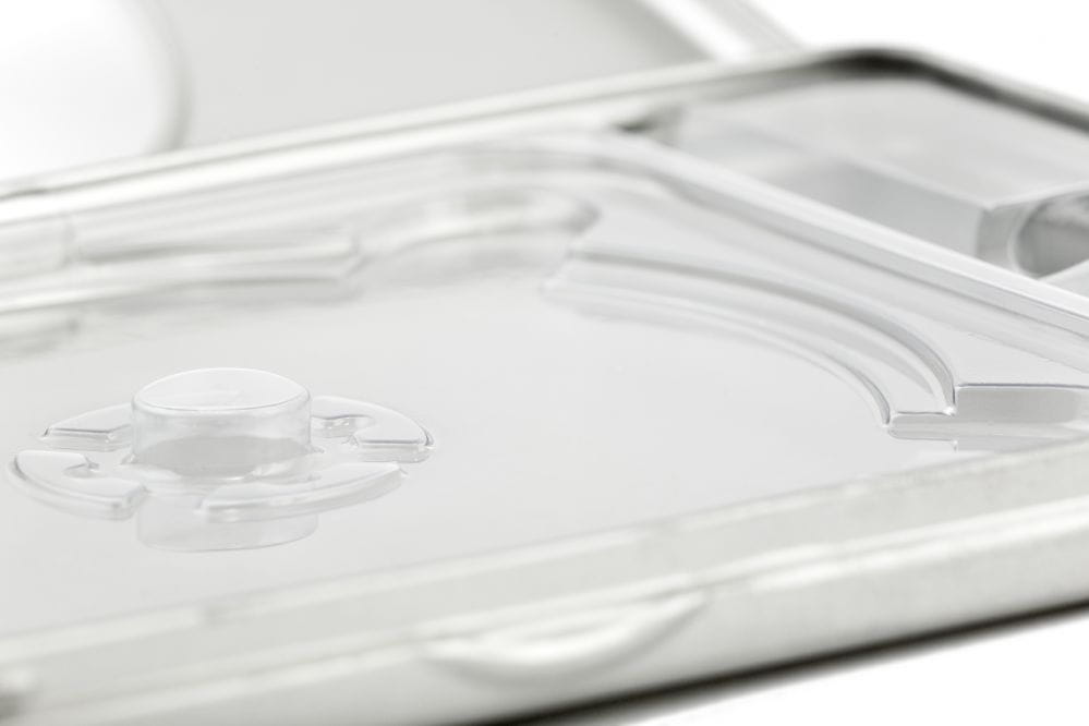 Detailaufnahme einer geöffneten DVD-Metalldose mit transparentem Kunststofftray und zentralem Disc-Halter, silberfarben, auf weißem Hintergrund fotografiert.
